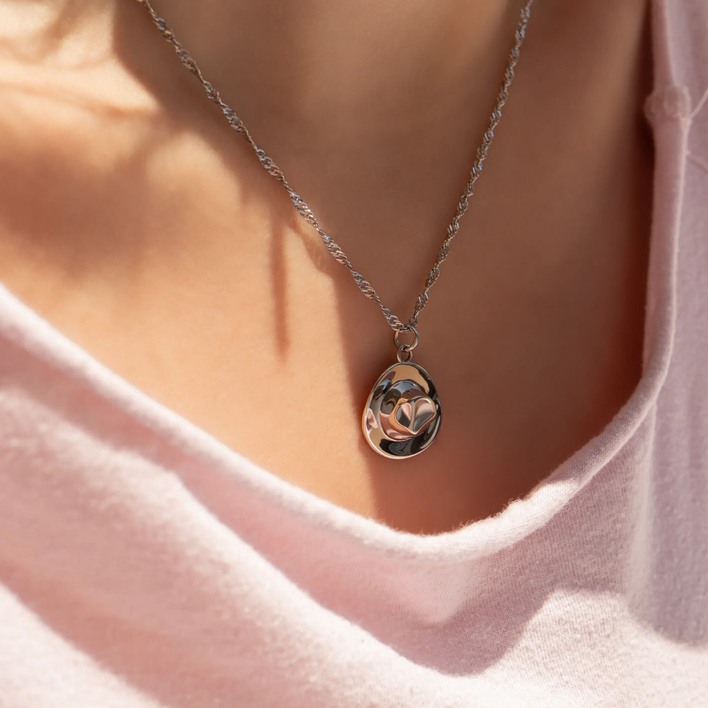 Necklace with a cowboy hat pendant worn by a person in a pink shirt