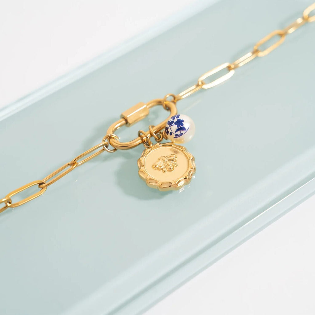 Gold bracelet with two charms on a light blue background