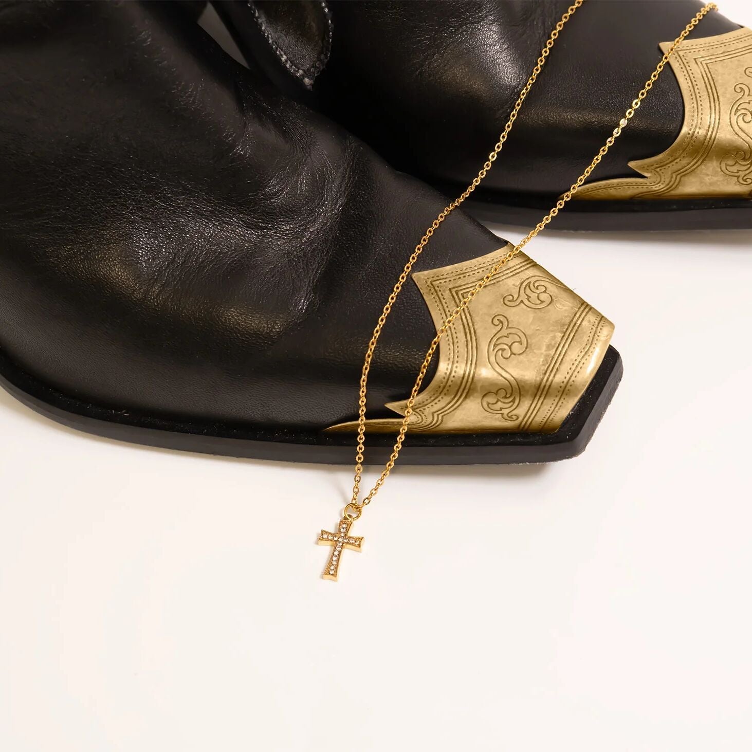 Gold necklace with a cross pendant on a black cowboy boots with gold accents.