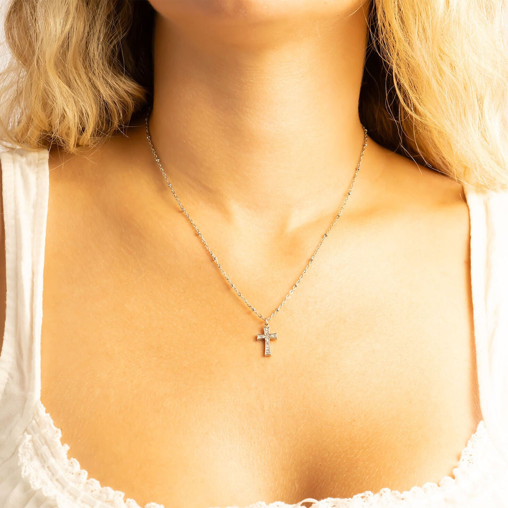 Necklace with a cross pendant worn by a person with blonde hair.