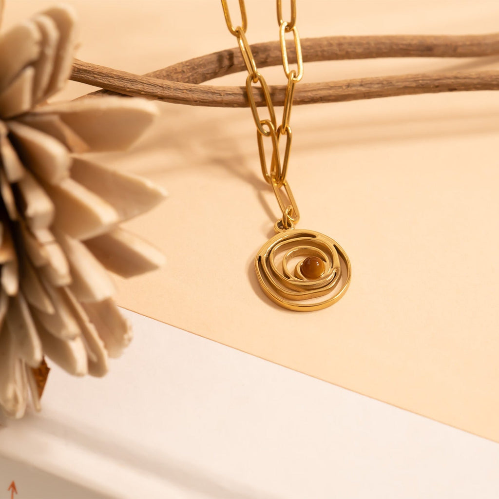 Gold chain necklace with a circular pendant on a beige background