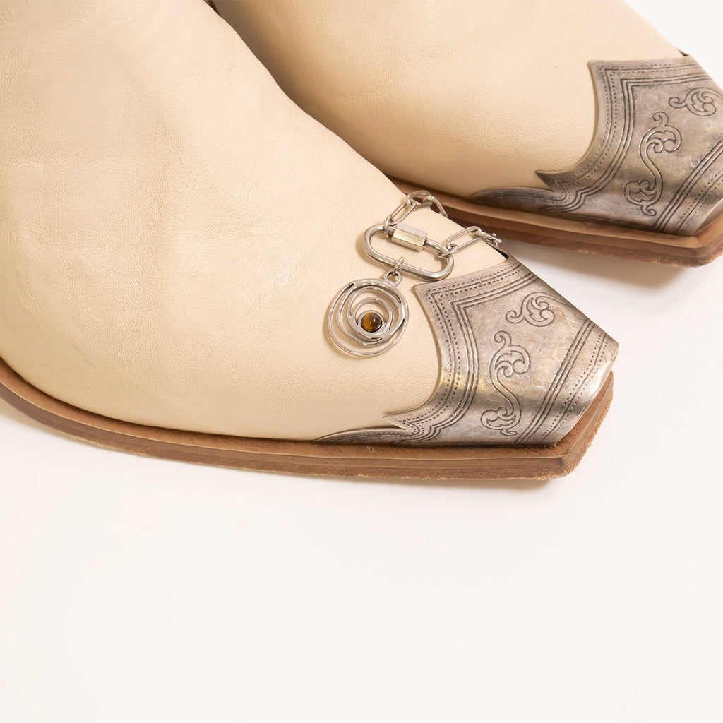 Beige shoe with decorative silver heel and white background