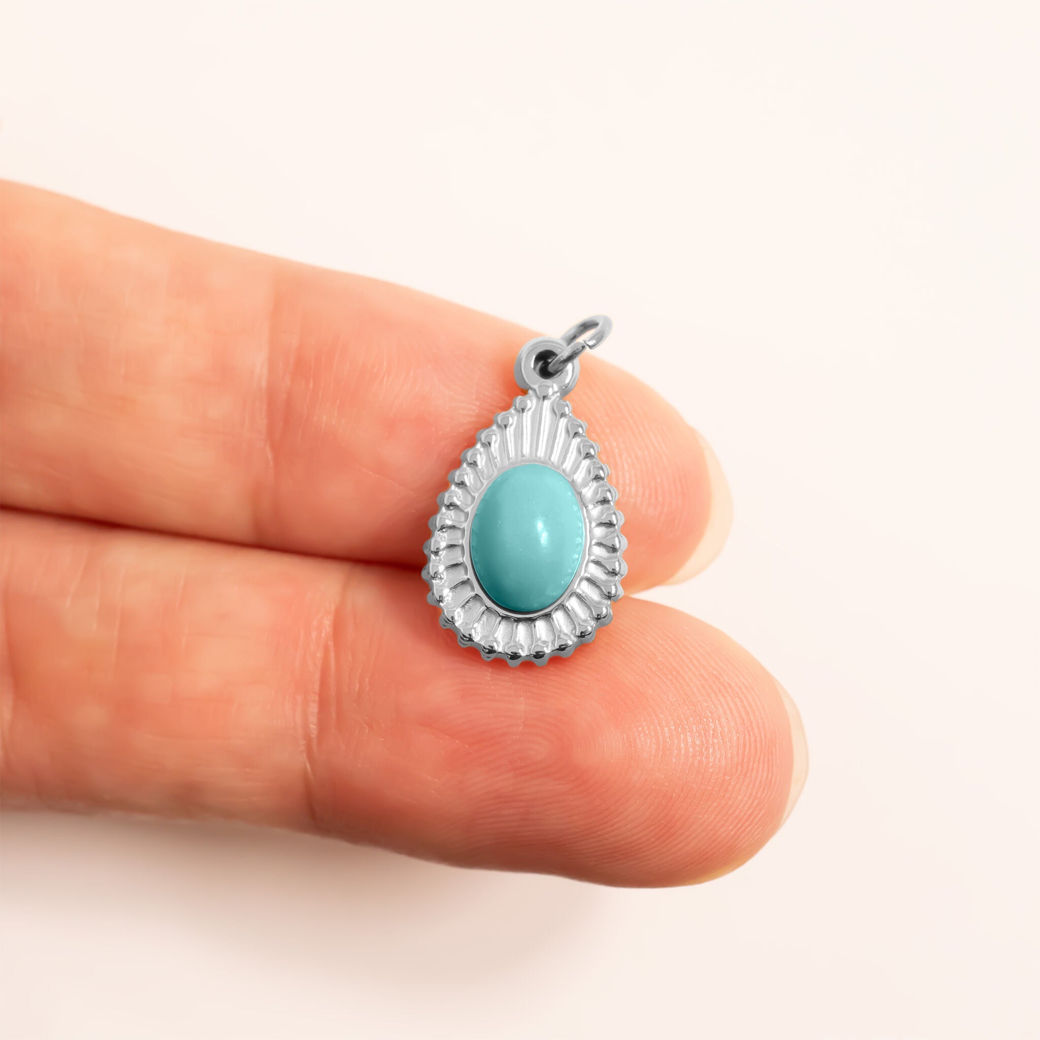Turquoise stone pendant held between two fingers for scale against a white background
