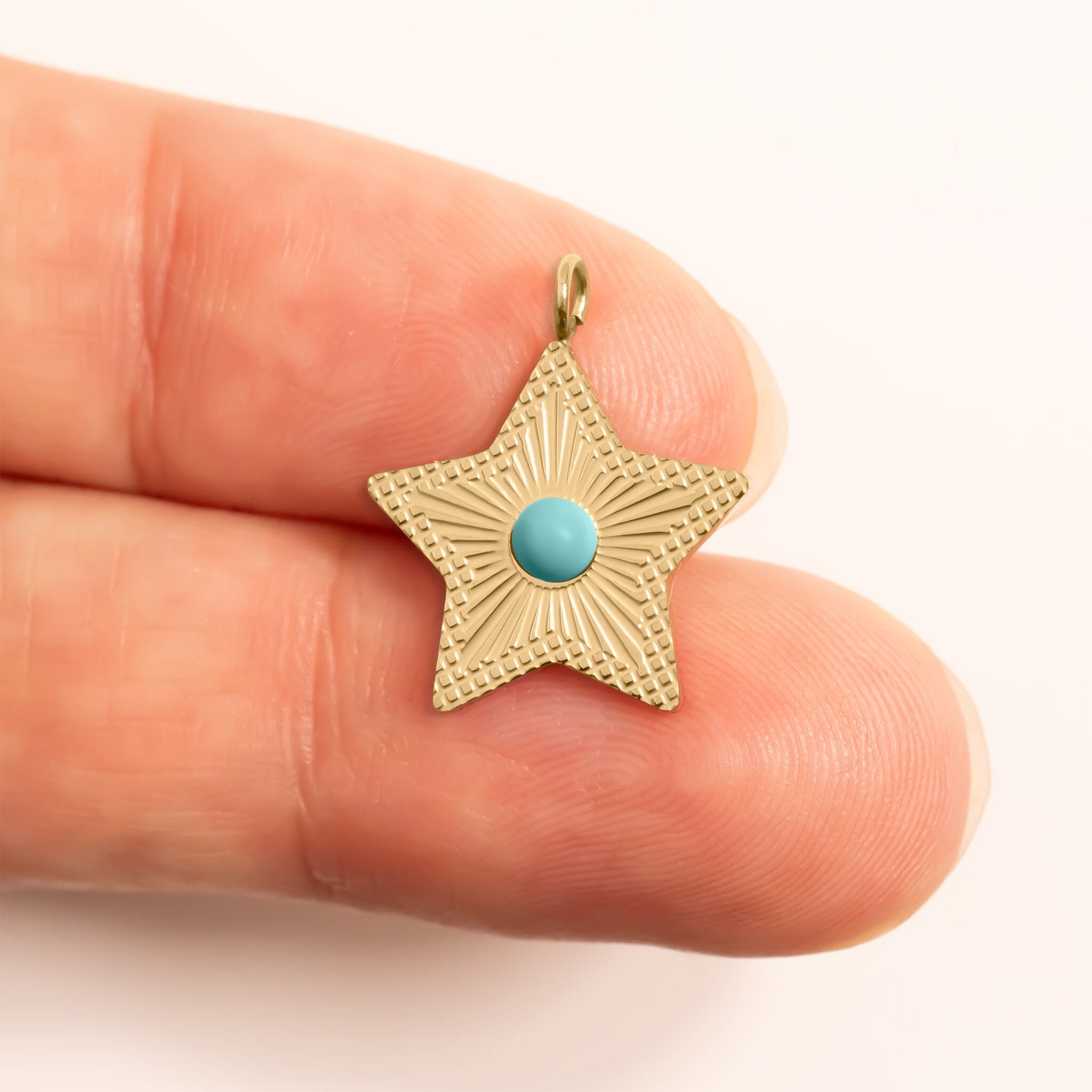 Gold star-shaped pendant with a turquoise stone held between two fingers for scale  on a white background