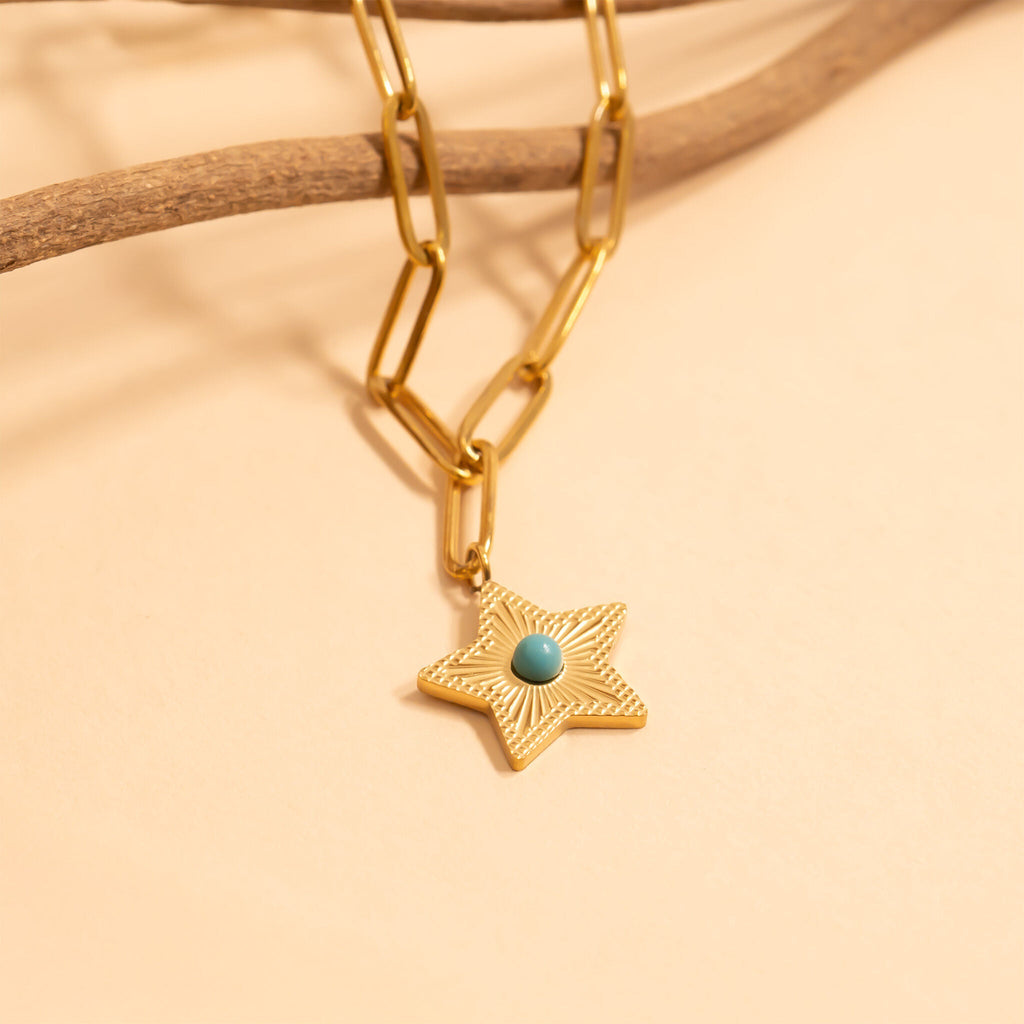 Gold chain necklace with a star-shaped pendant featuring a turquoise bead on a beige background