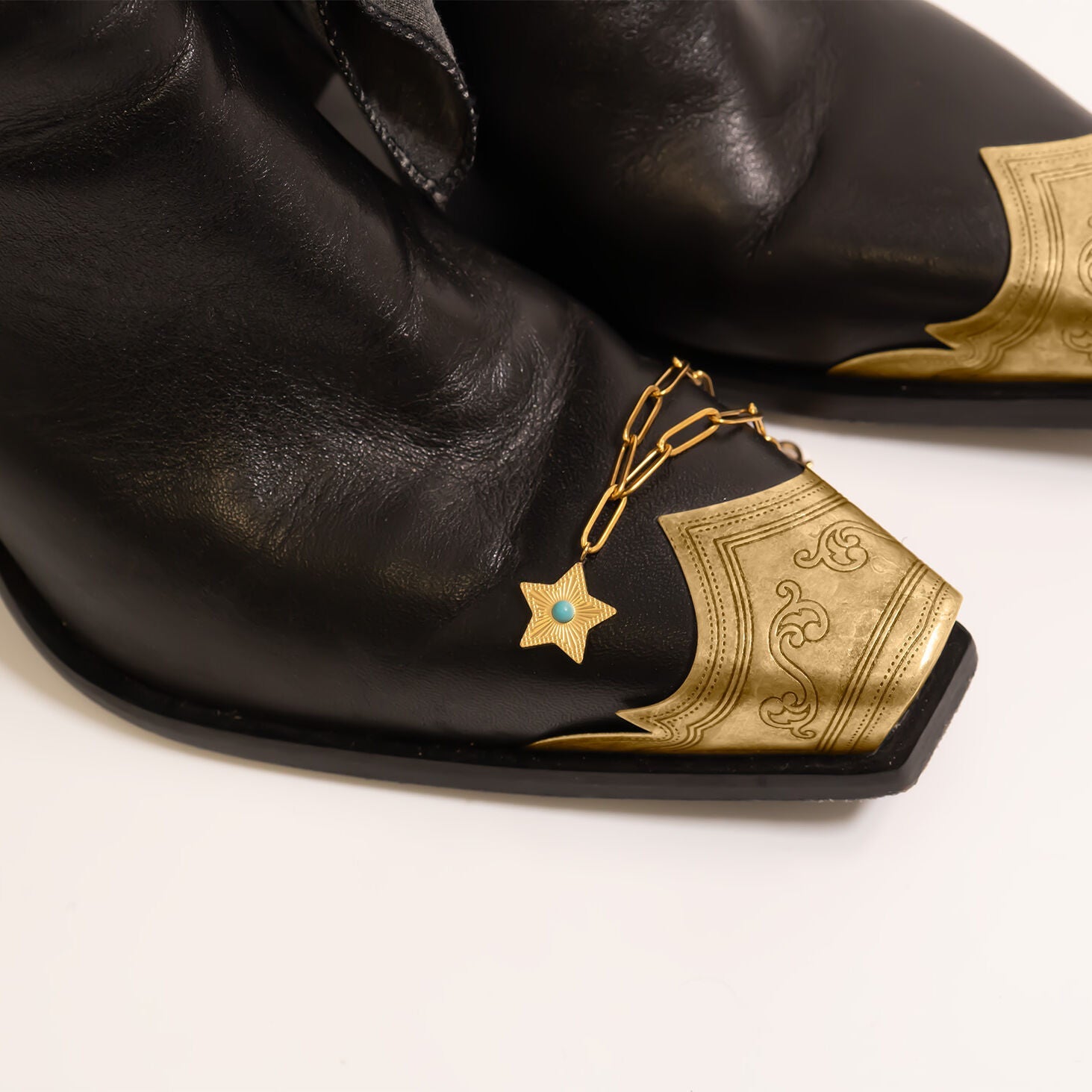 Turquoise Star Charm near gold toed black leather cowboy boots on a white background
