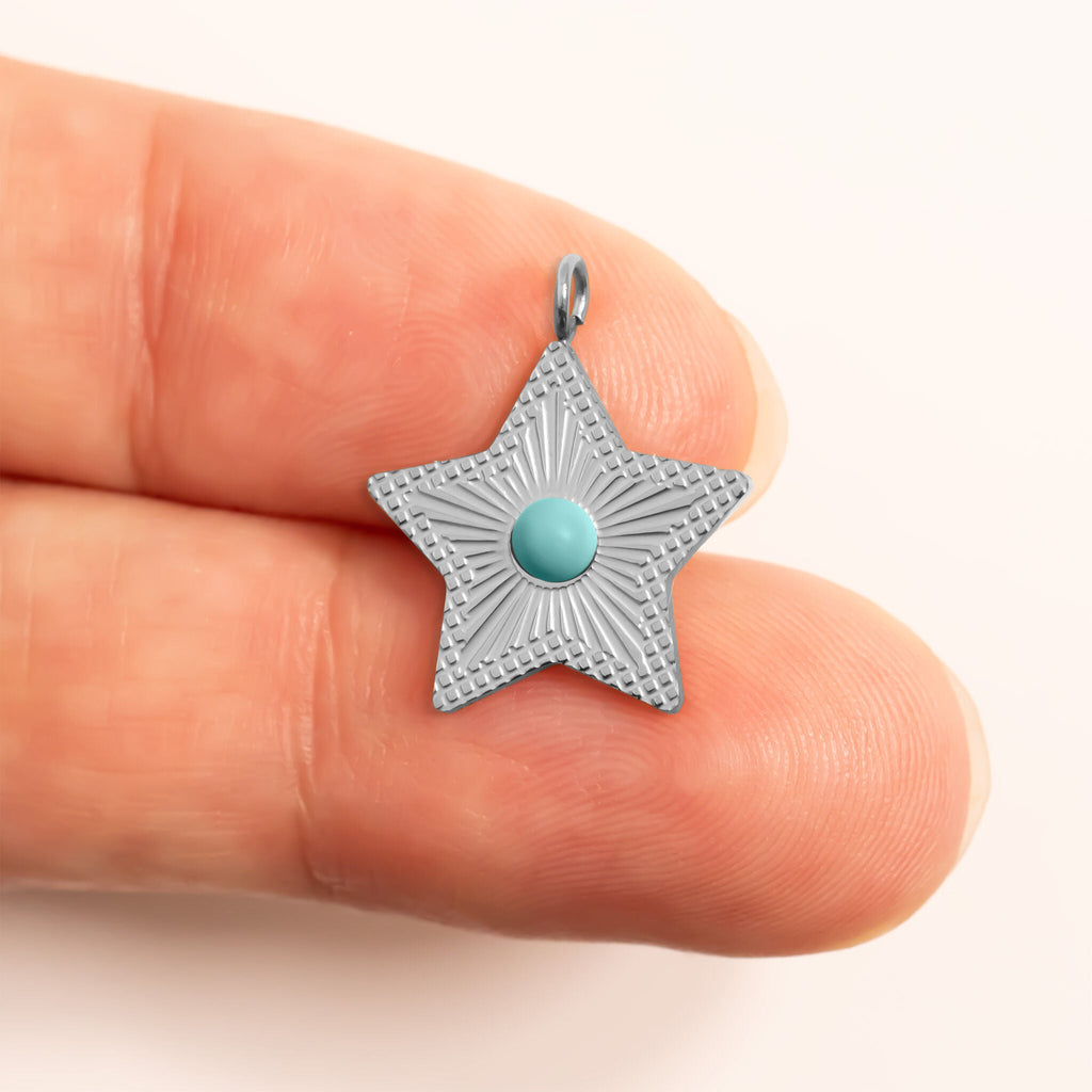 Silver star-shaped pendant with a turquoise gemstone held between fingers for scale on a white background
