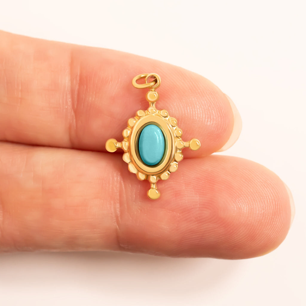 Gold pendant with a turquoise stone held between two fingers for scale on a white background