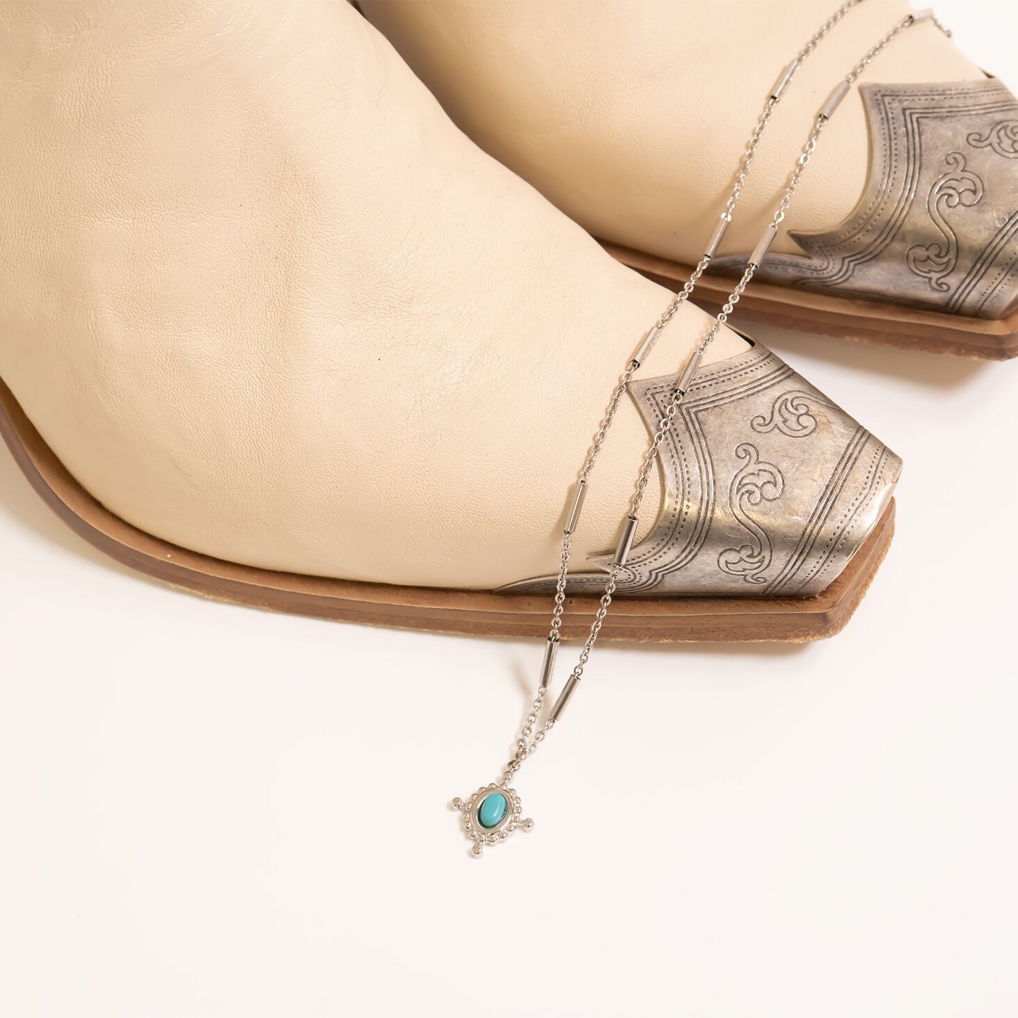 Necklace with turquoise compass pendant draped over a beige cowboy shoe