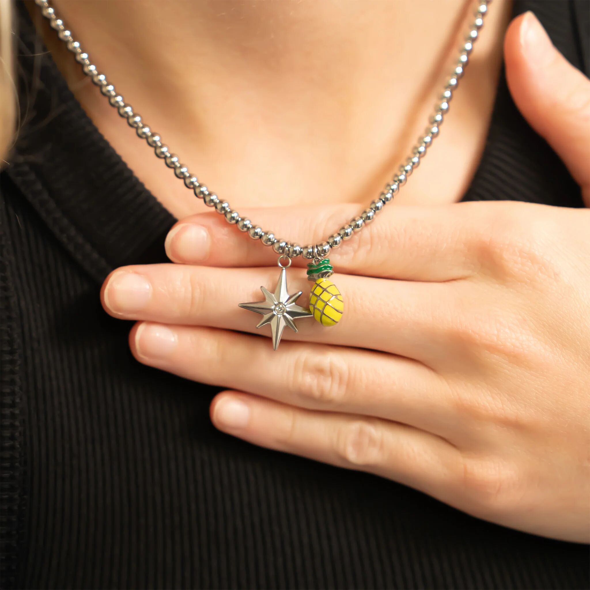Close-up of a beaded necklace with star and pineapple charms held by a hand against a black background