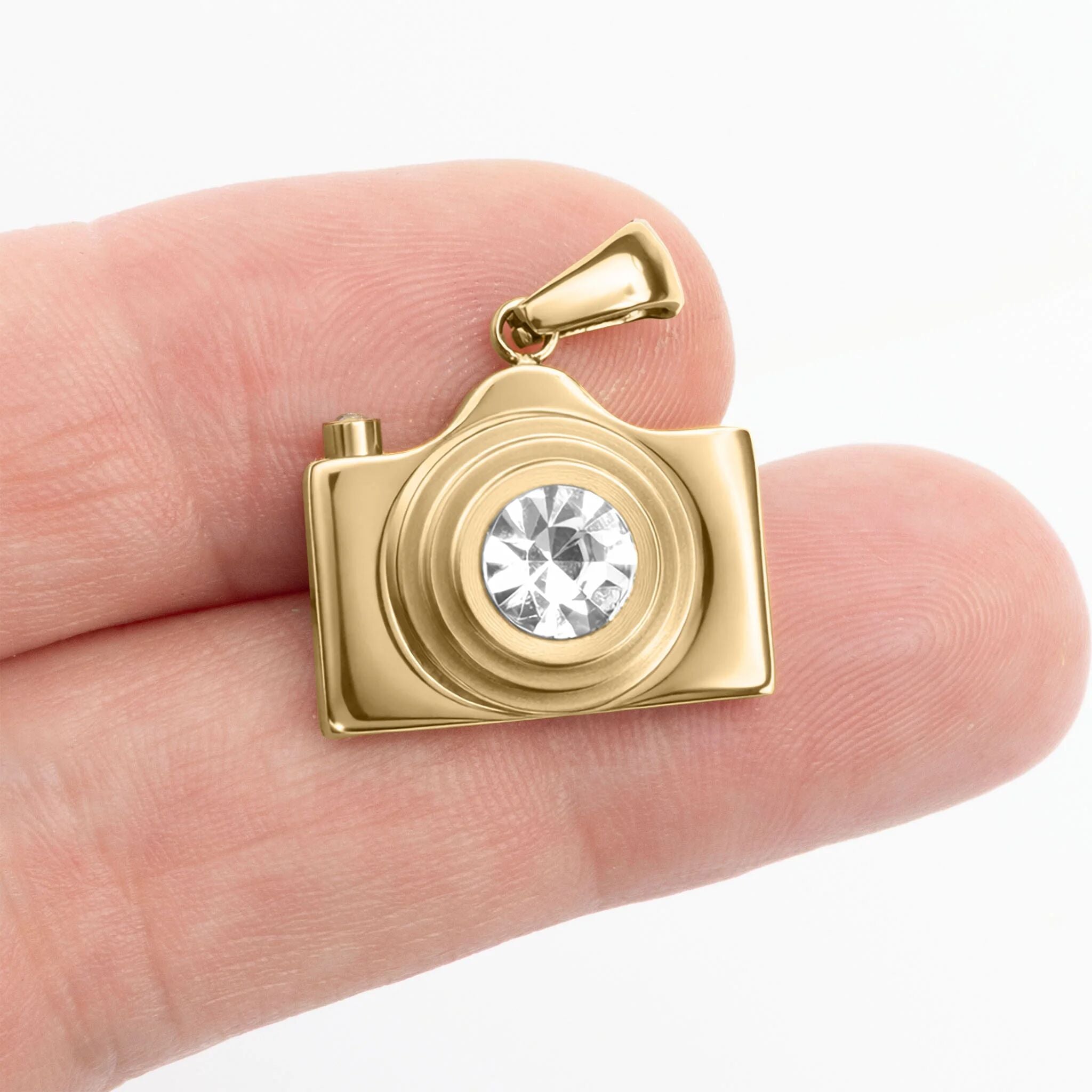 Gold camera-shaped pendant with a clear gemstone held between fingers on a white background