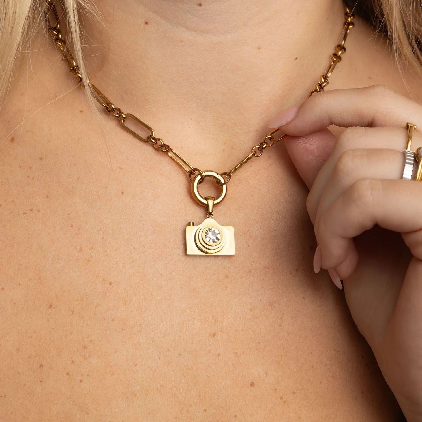 Gold necklace with a camera-shaped pendant worn by a person