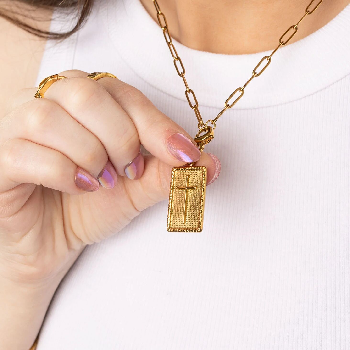 Gold necklace with a cross pendant held by a person against a white background