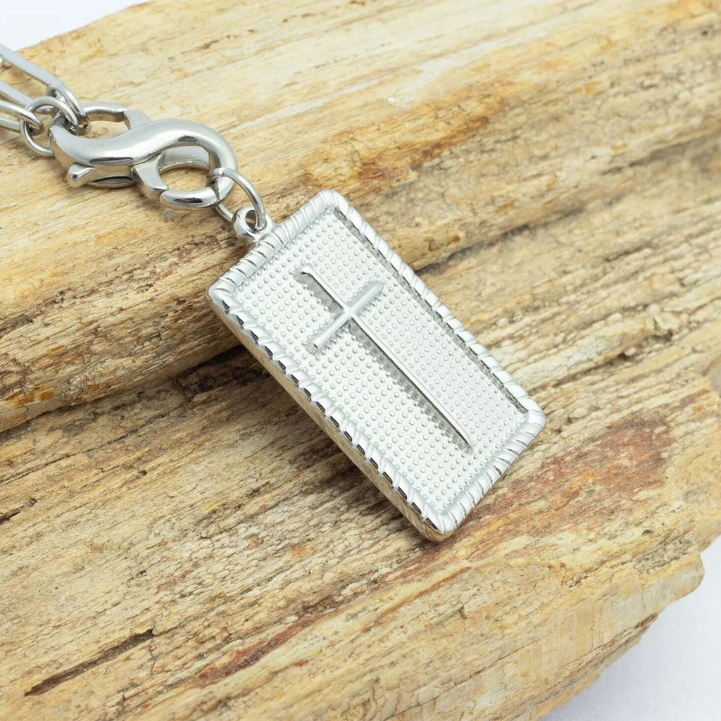 Silver cross pendant on a chain against a wooden background