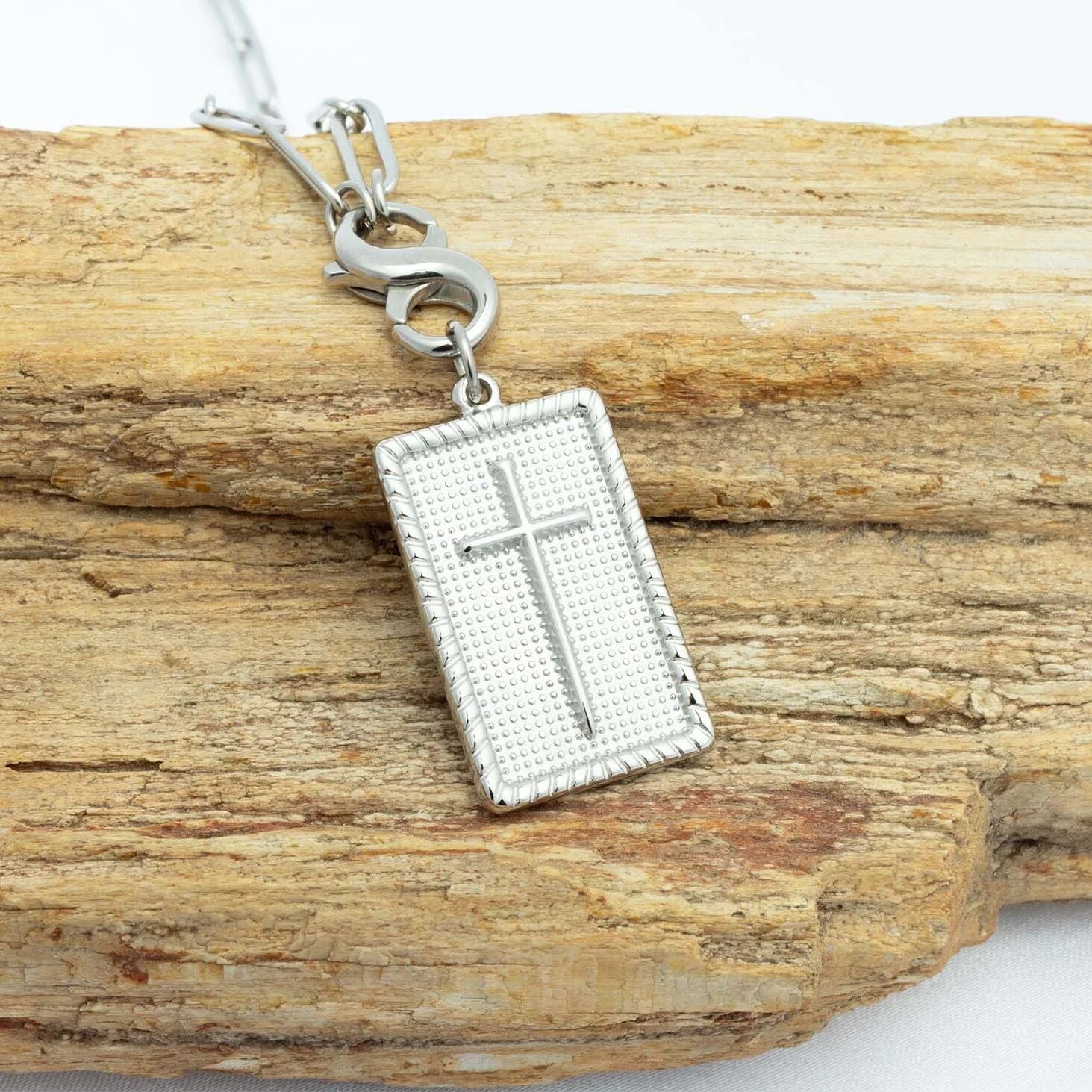 Silver cross pendant on a chain, placed on a wooden surface