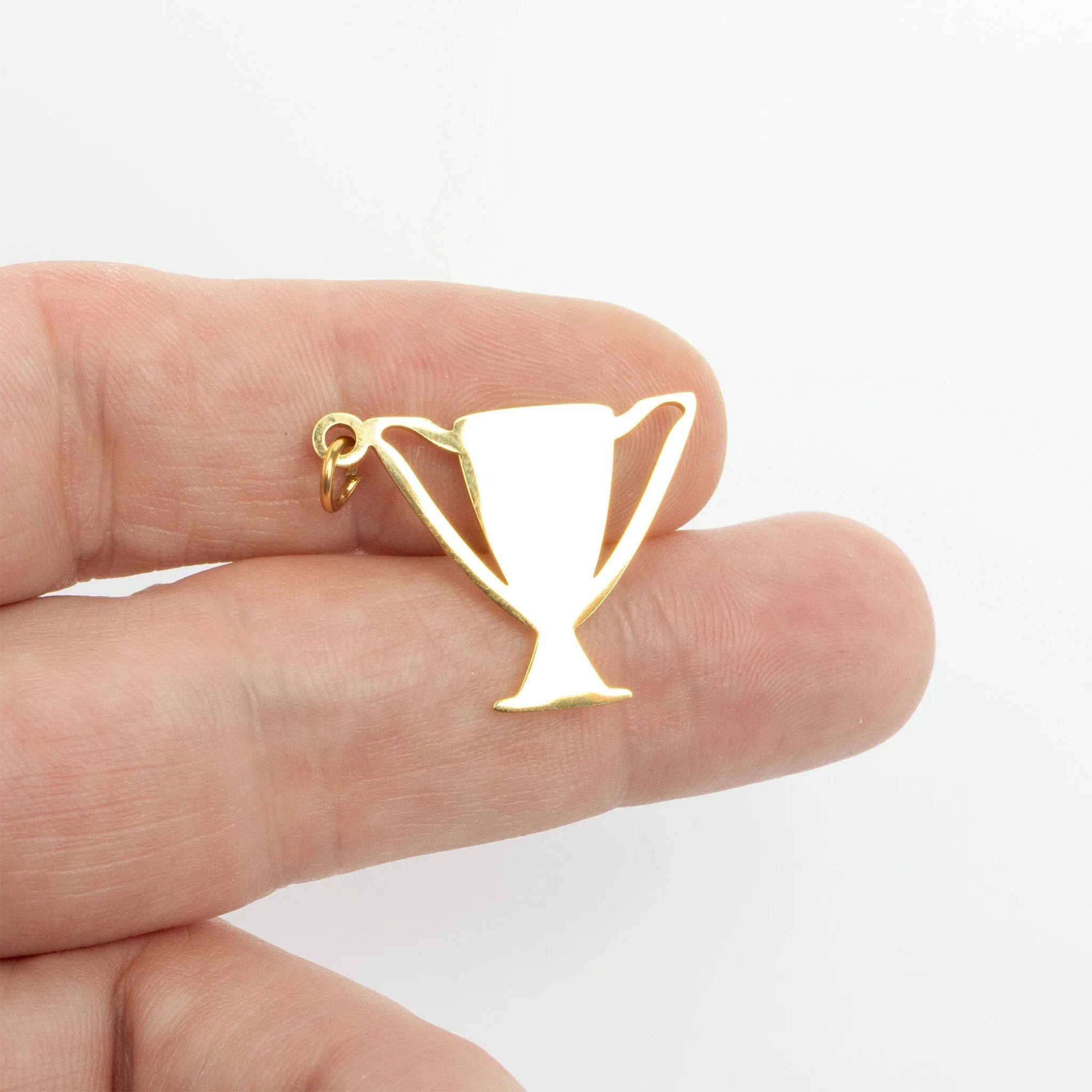 Gold trophy-shaped pendant held between fingers on a white background