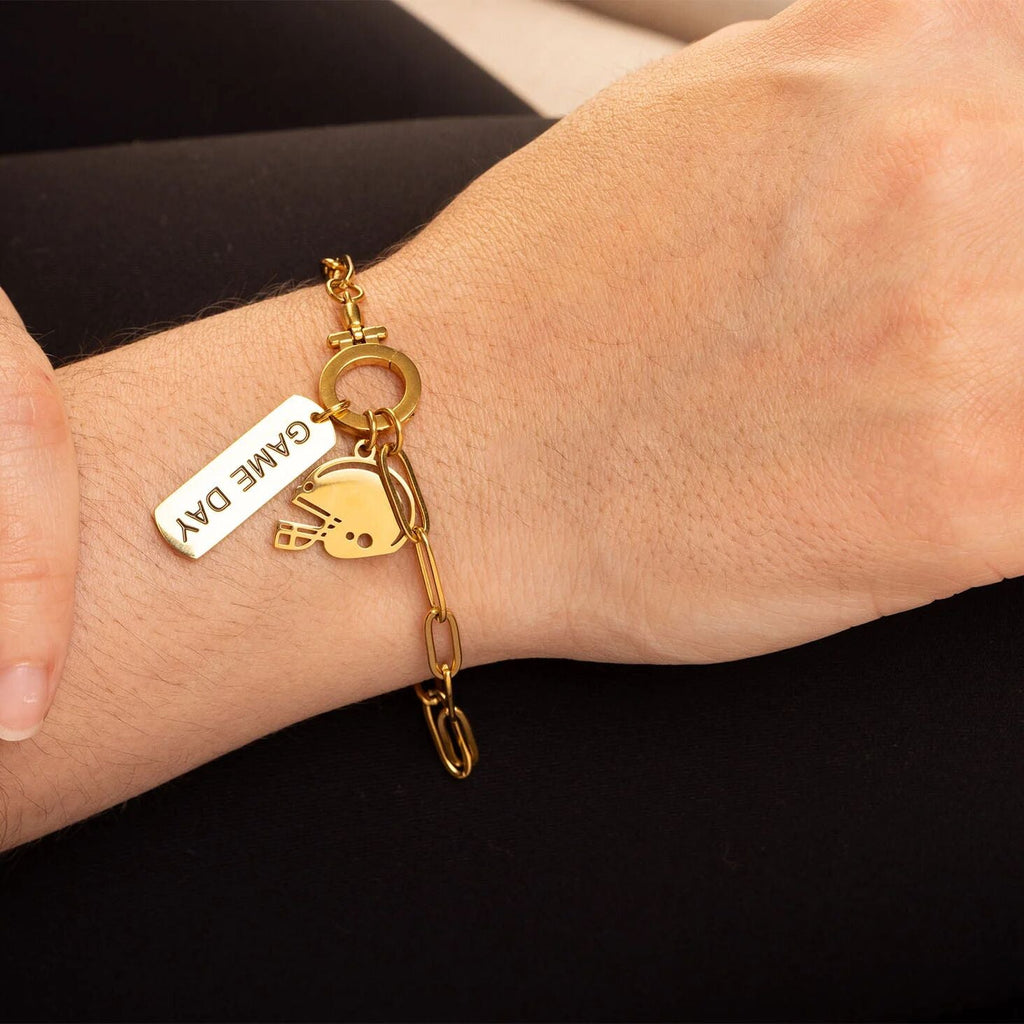 Gold bracelet with 'Game Day' charm on a wrist against a black background