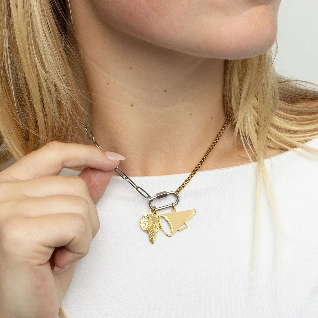 Person adjusting a gold necklace with a unique pendant on a plain background
