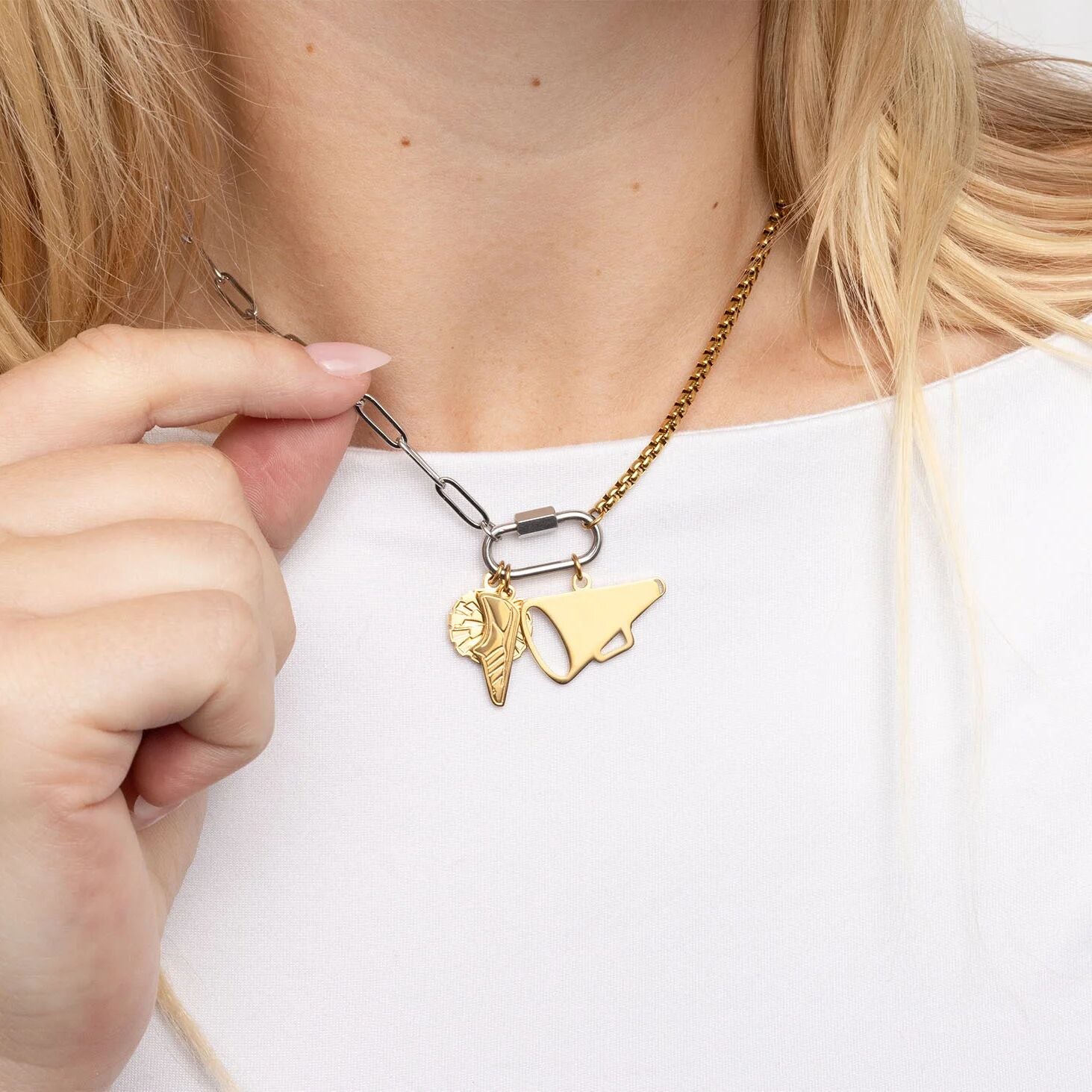 Gold necklace with two charms being adjusted by a hand on a white background