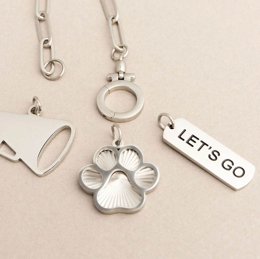 Silver keychain with paw print and 'LET'S GO' tag on a beige background