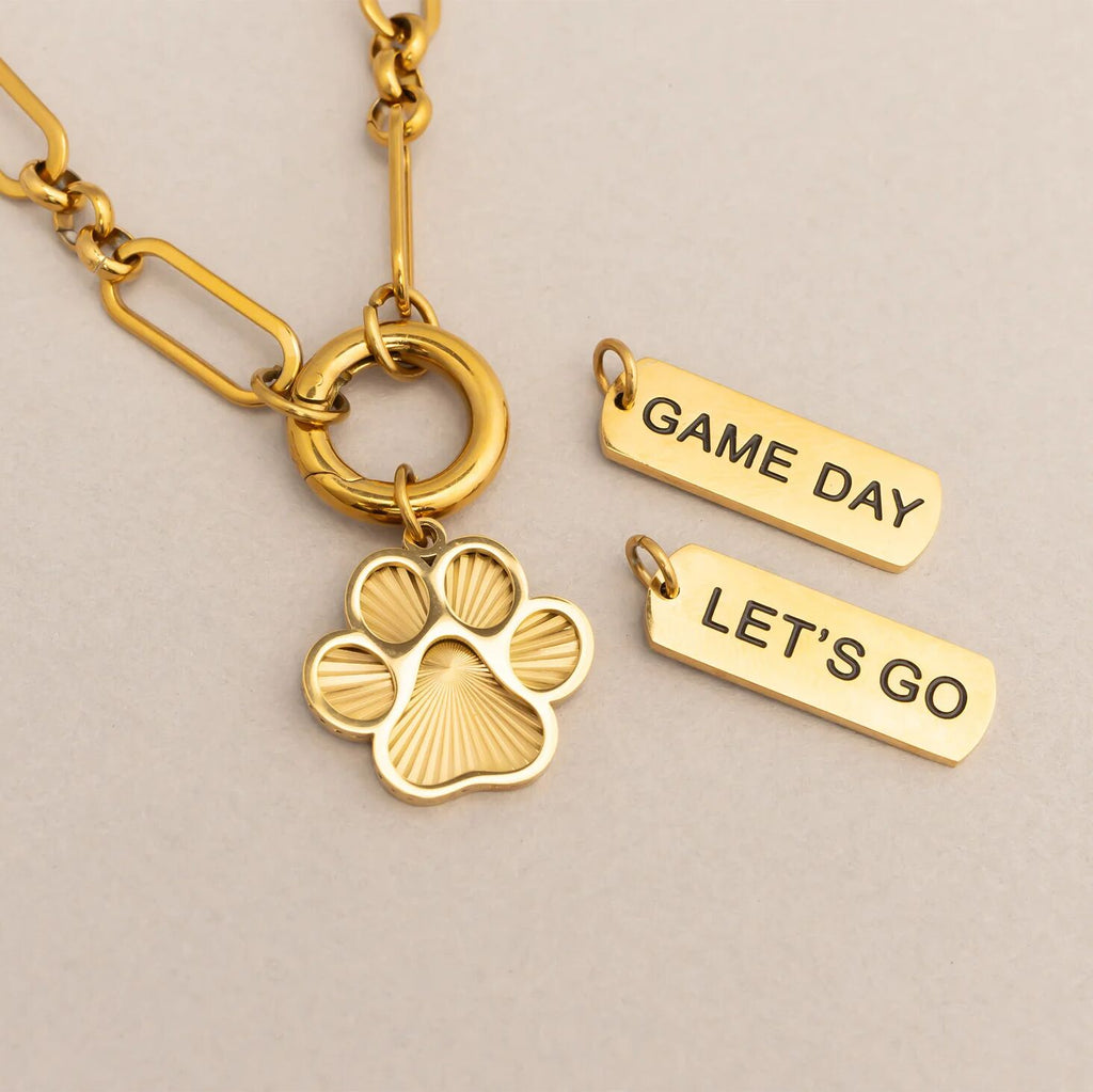 Gold keychain with paw charm and 'Game Day Let's Go' tags on a beige background