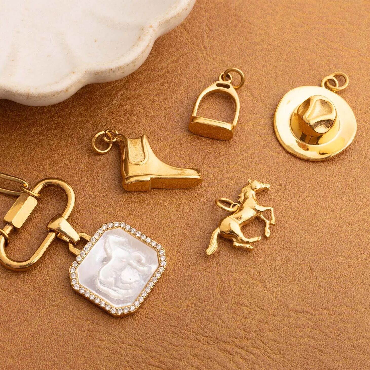 Collection of gold equestrian charms including a boot, stirrup, horse, and on a brown surface.