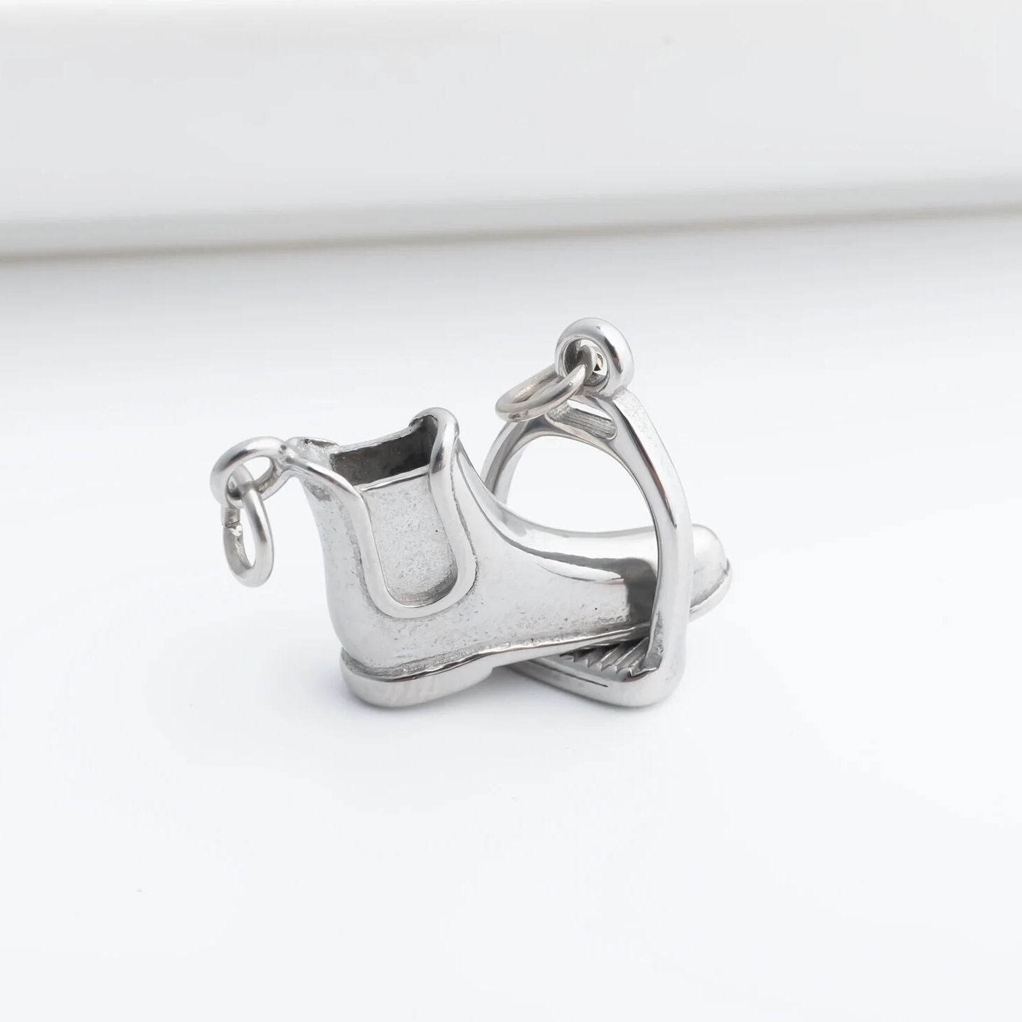 Silver equestrian boot and stirrup charm on a white background