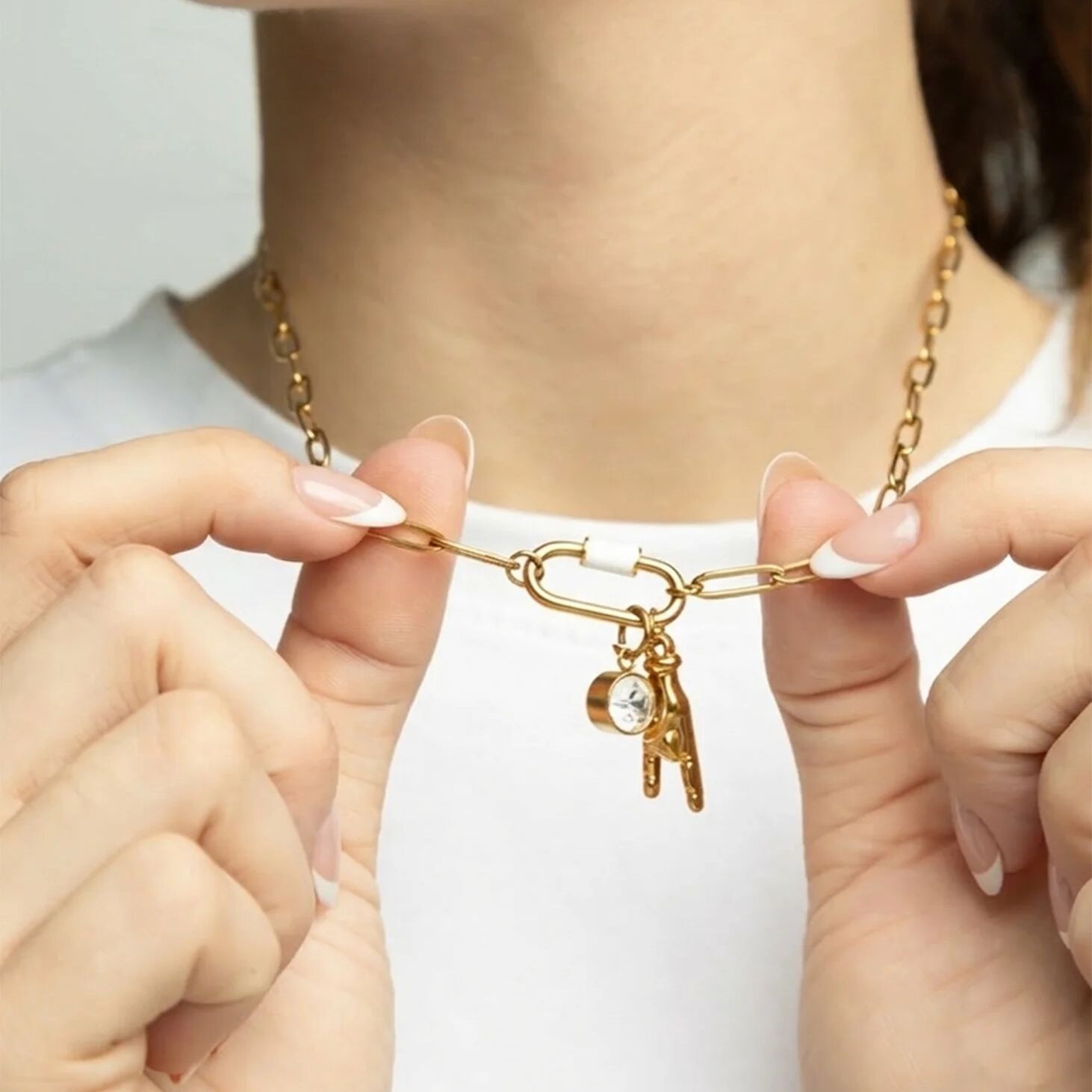 Gold necklace with charms held by hands against a white background