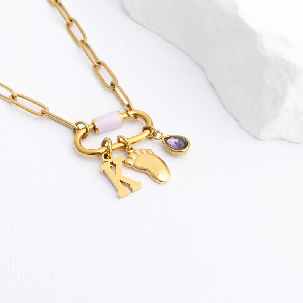 Gold necklace with a baby foot, birthstone, and initial charms on a white background