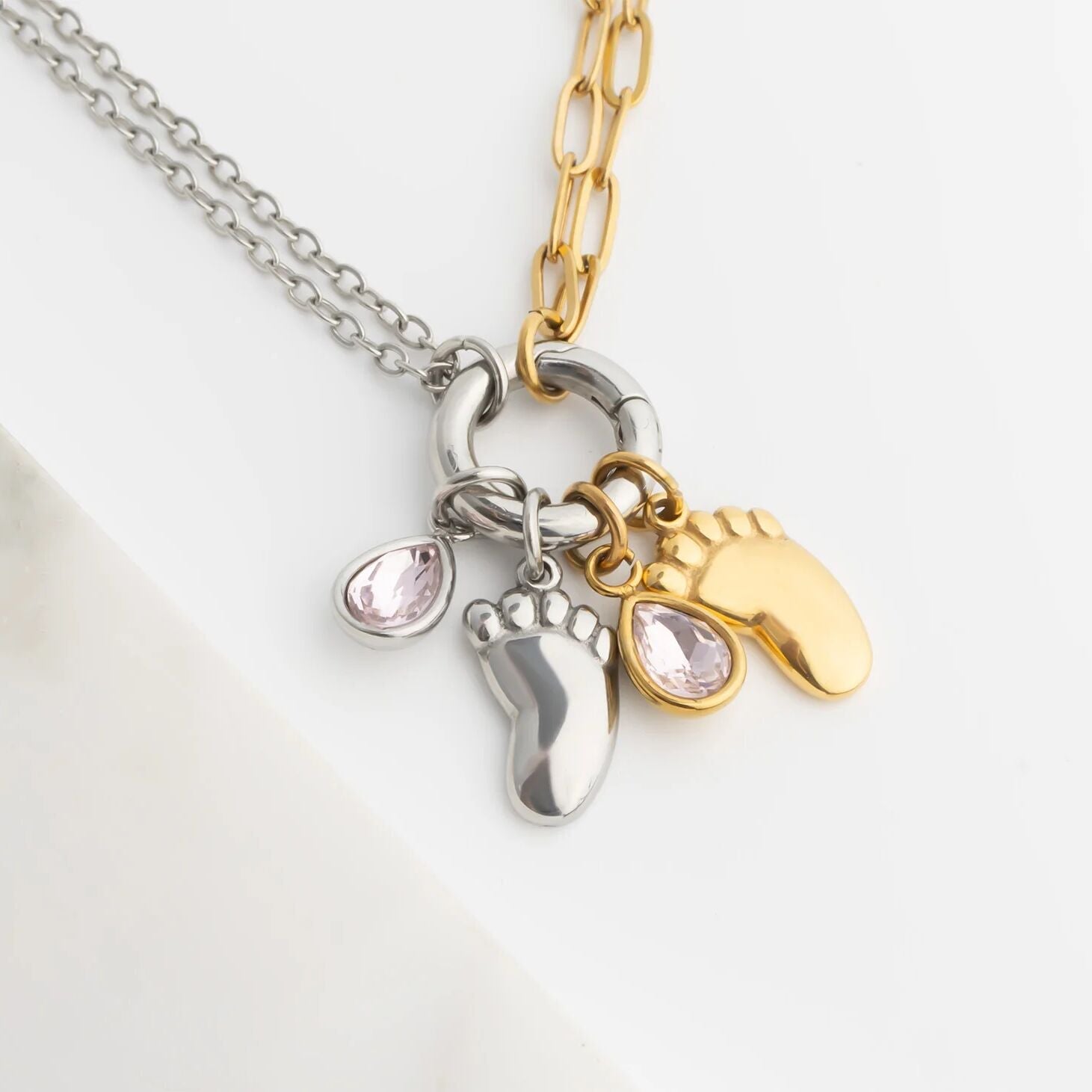 Two toned necklace with two foot charm, two pink teardrop charm on a white background