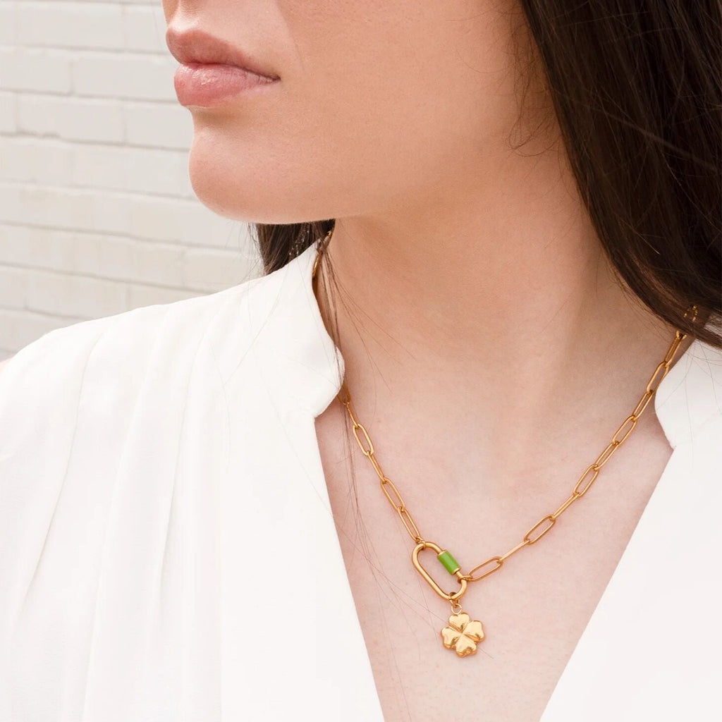 Gold necklace with a green pendant worn by a person against a neutral background