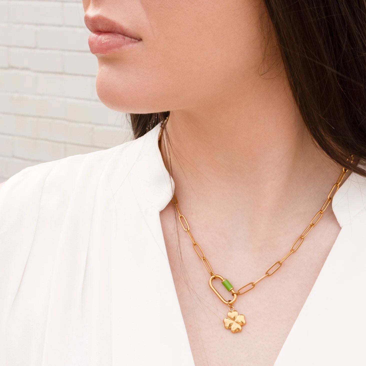 Gold necklace with a green pendant worn by a person against a neutral background