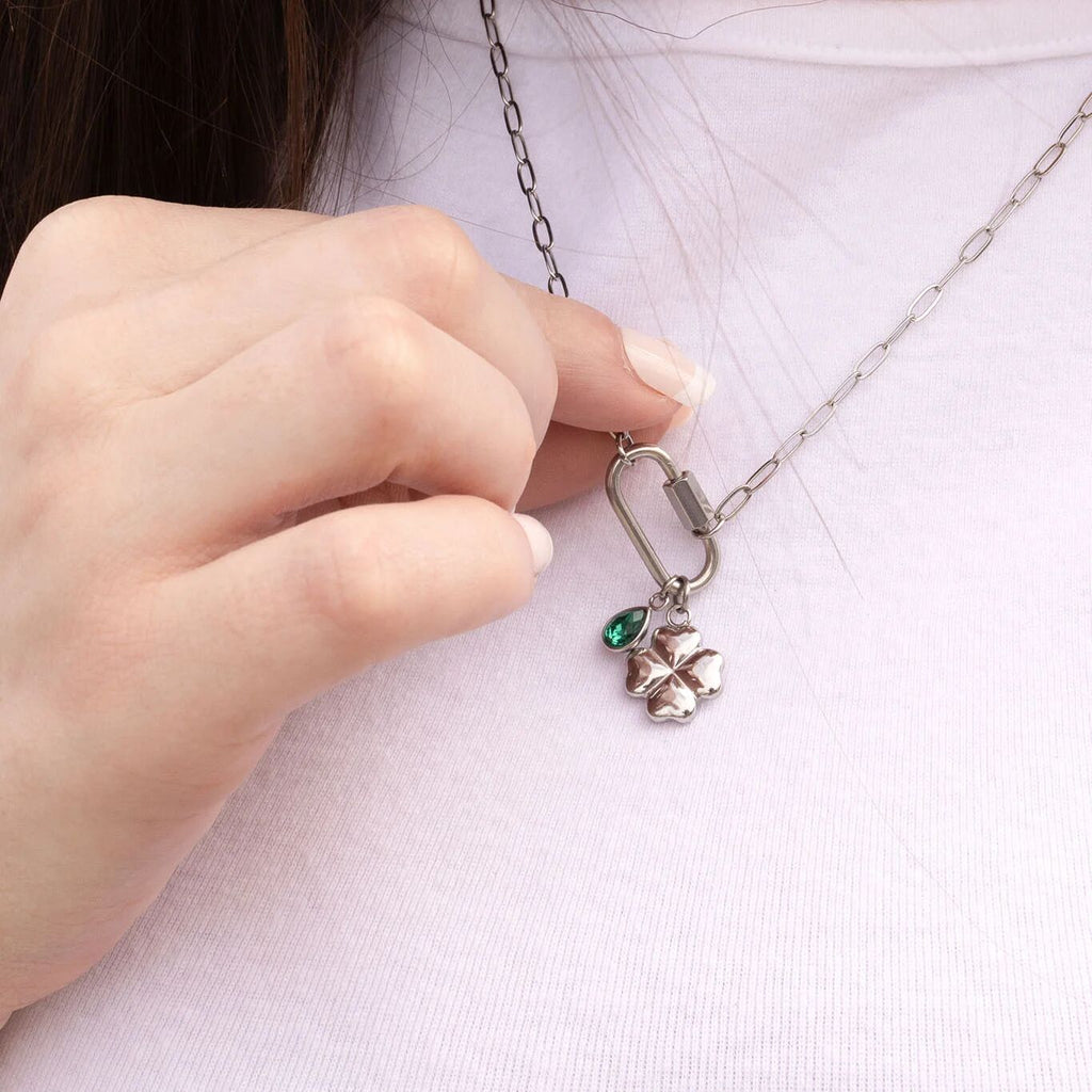 Hand holding a silver necklace with a clover pendant and green gemstone against a white background