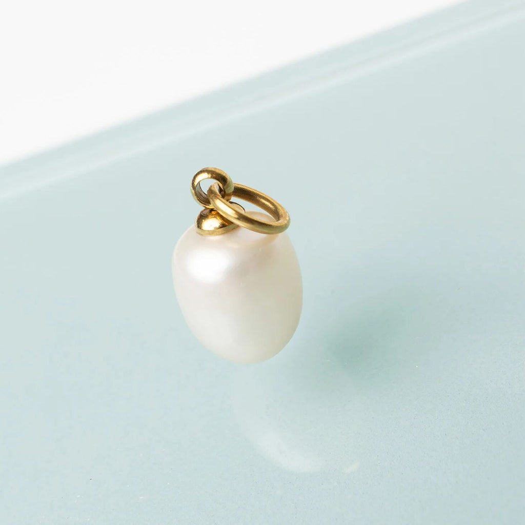 Pearl charm with gold ring on a light blue background