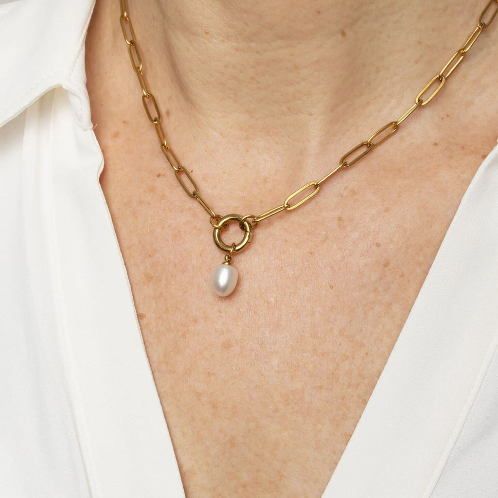 Gold chain necklace with a pearl pendant on a person wearing a white shirt.