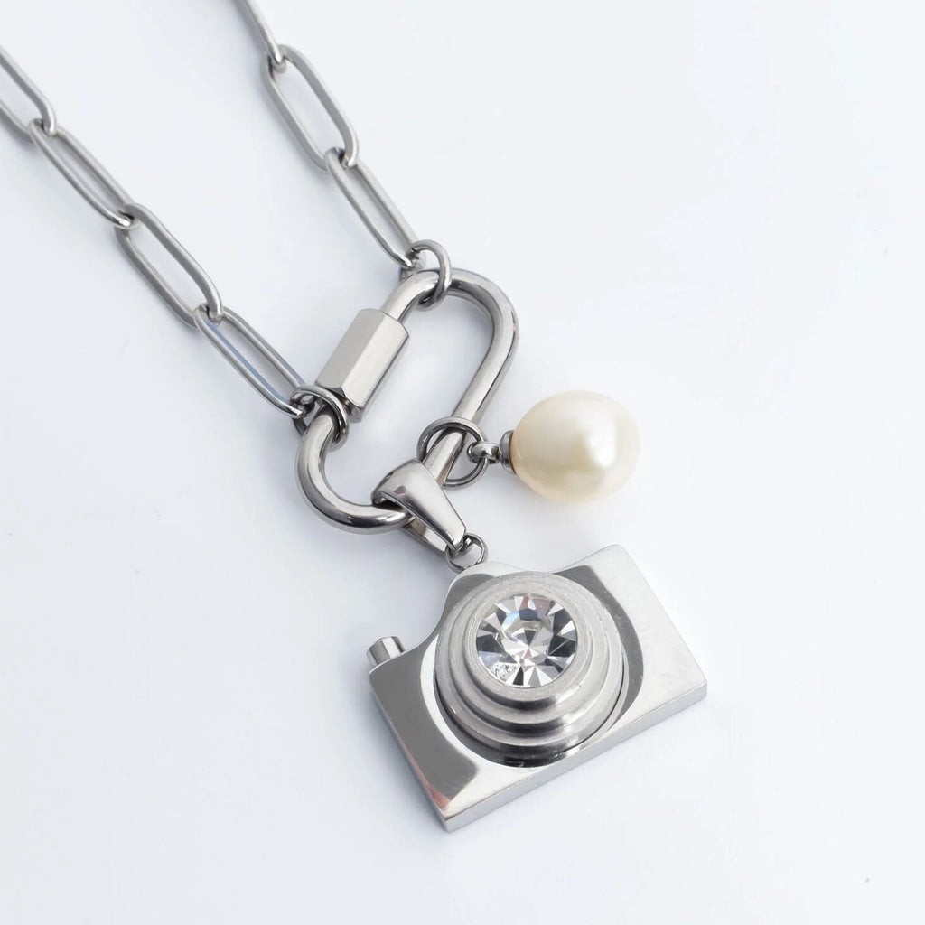 Silver necklace with a camera charm and pearl on a light gray background