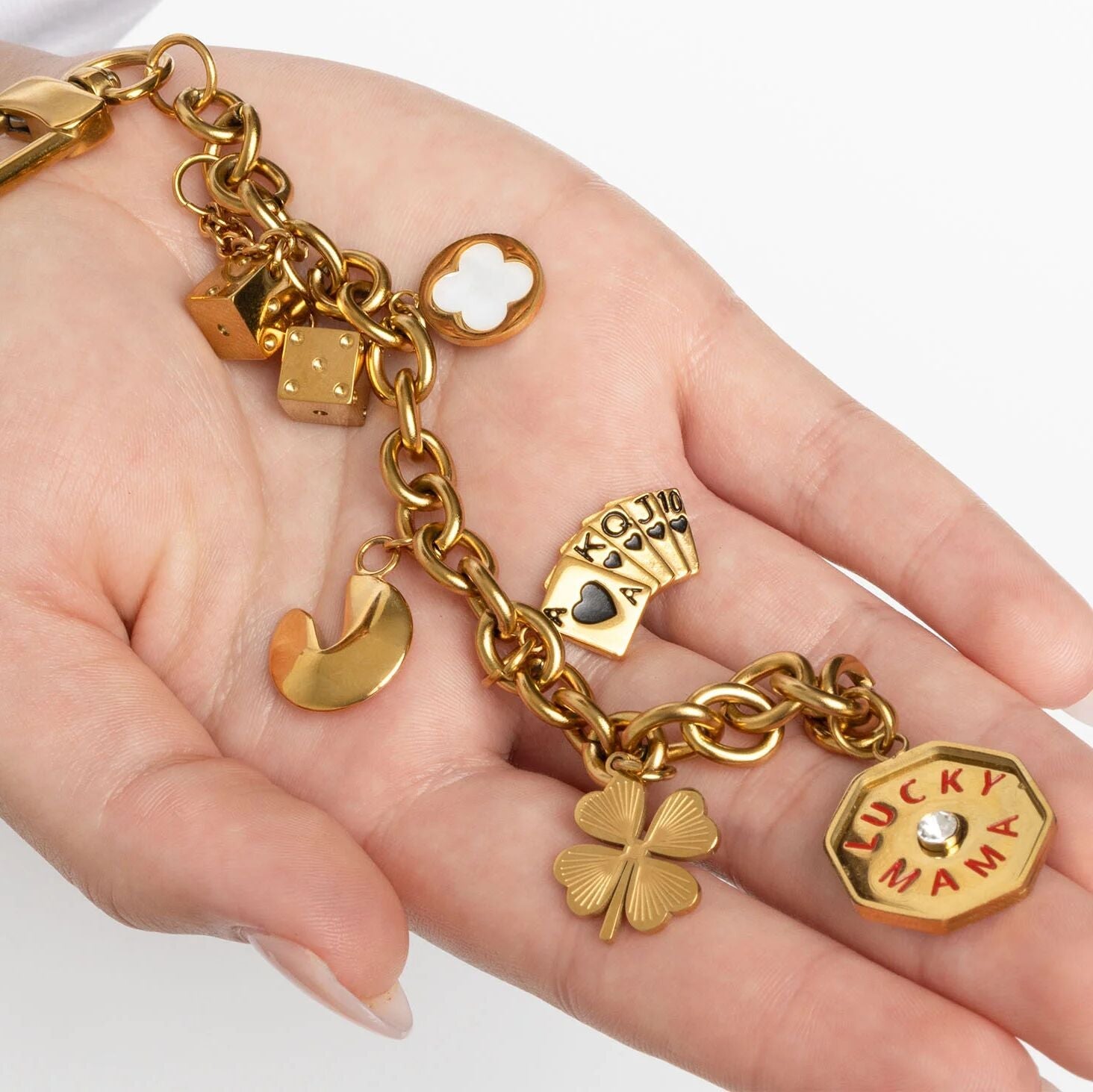Gold charm bracelet with various charms held in a hand on a white background