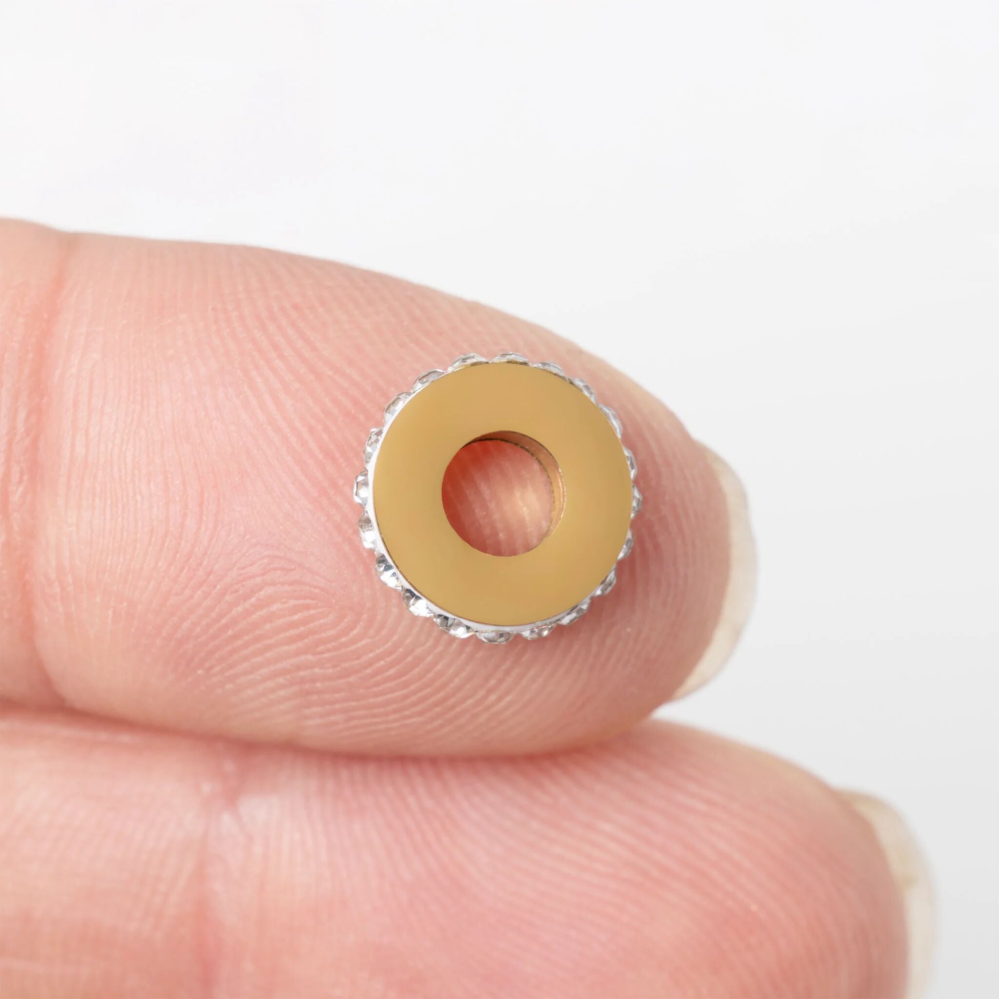 Gold stone spacer bead held between fingers against a white background