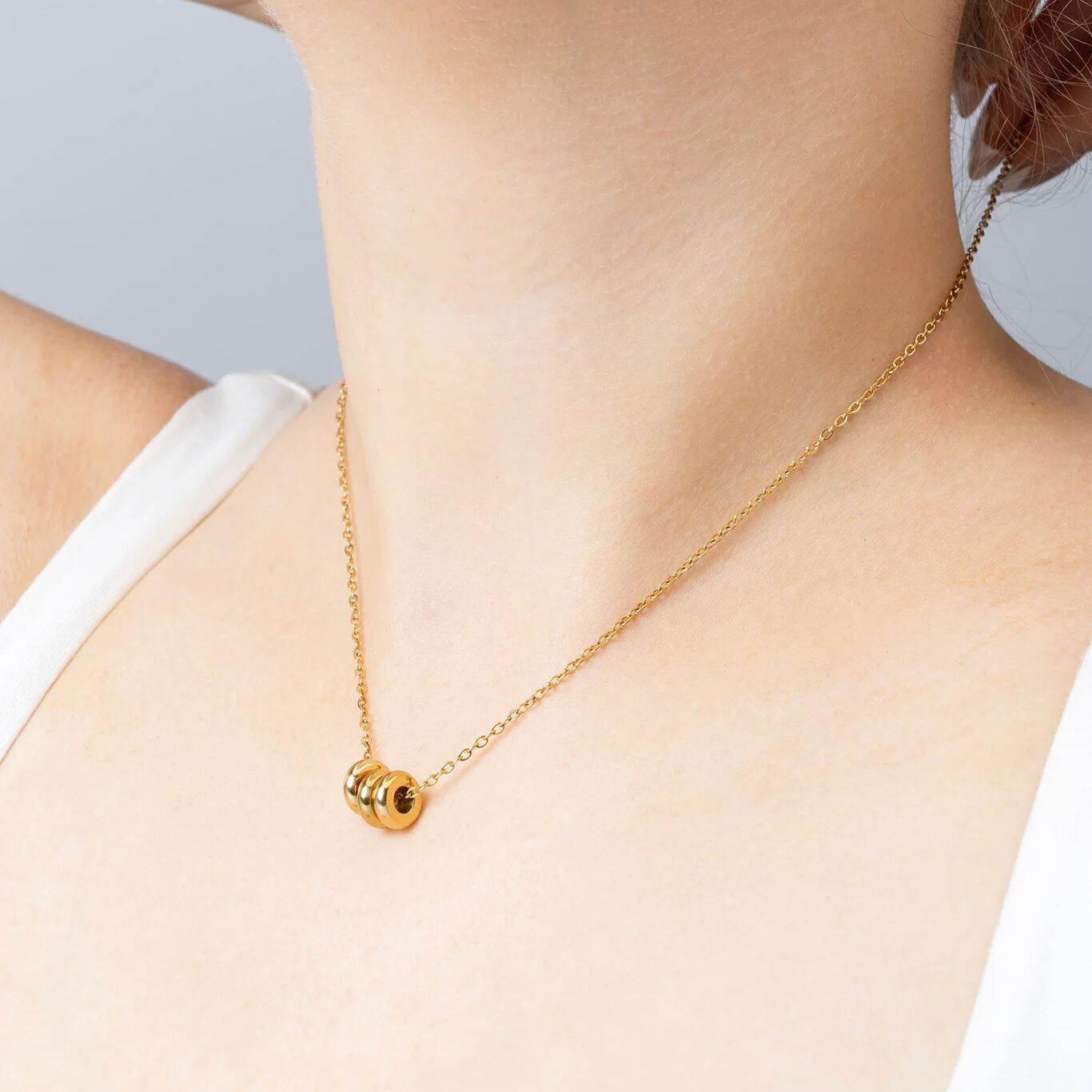 Gold necklace with a spacer beads on a person wearing a white top against a light gray background