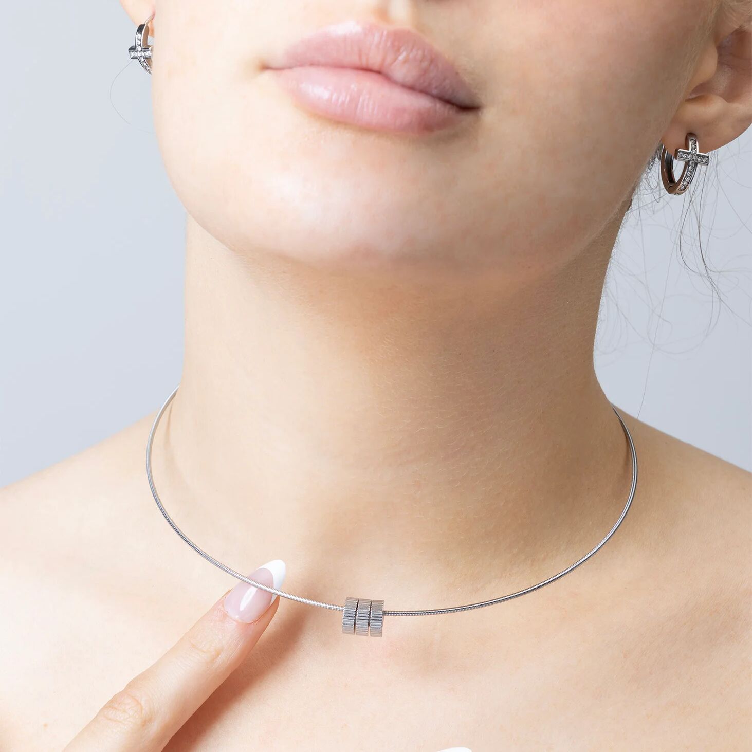 Close-up of a person wearing a silver necklace with fluted spacer beads on a neutral background