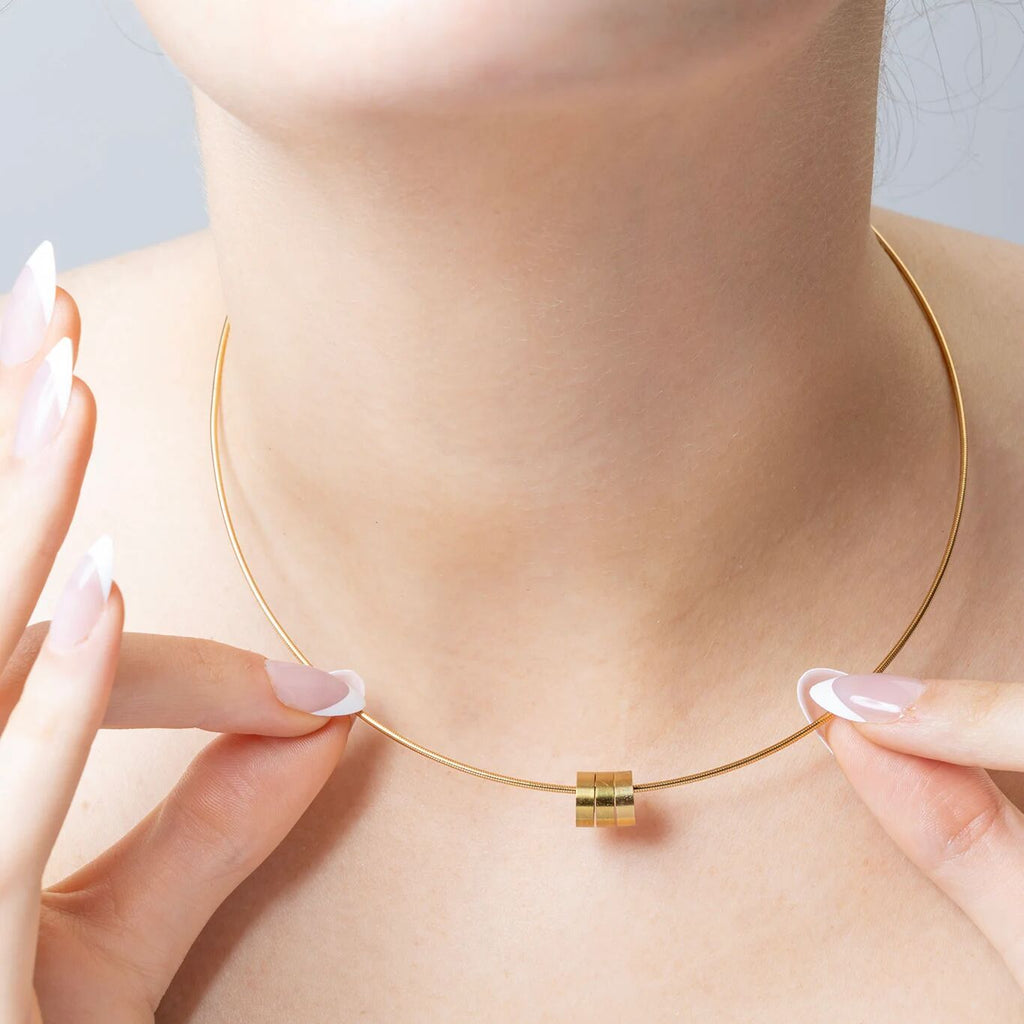 Gold necklace being worn on a person's neck with a neutral background