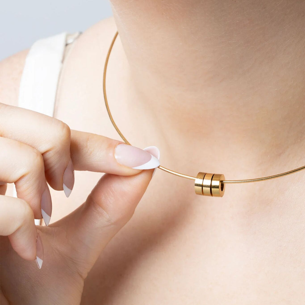 Gold necklace with spacer beads being adjusted on a person's neck with a neutral background