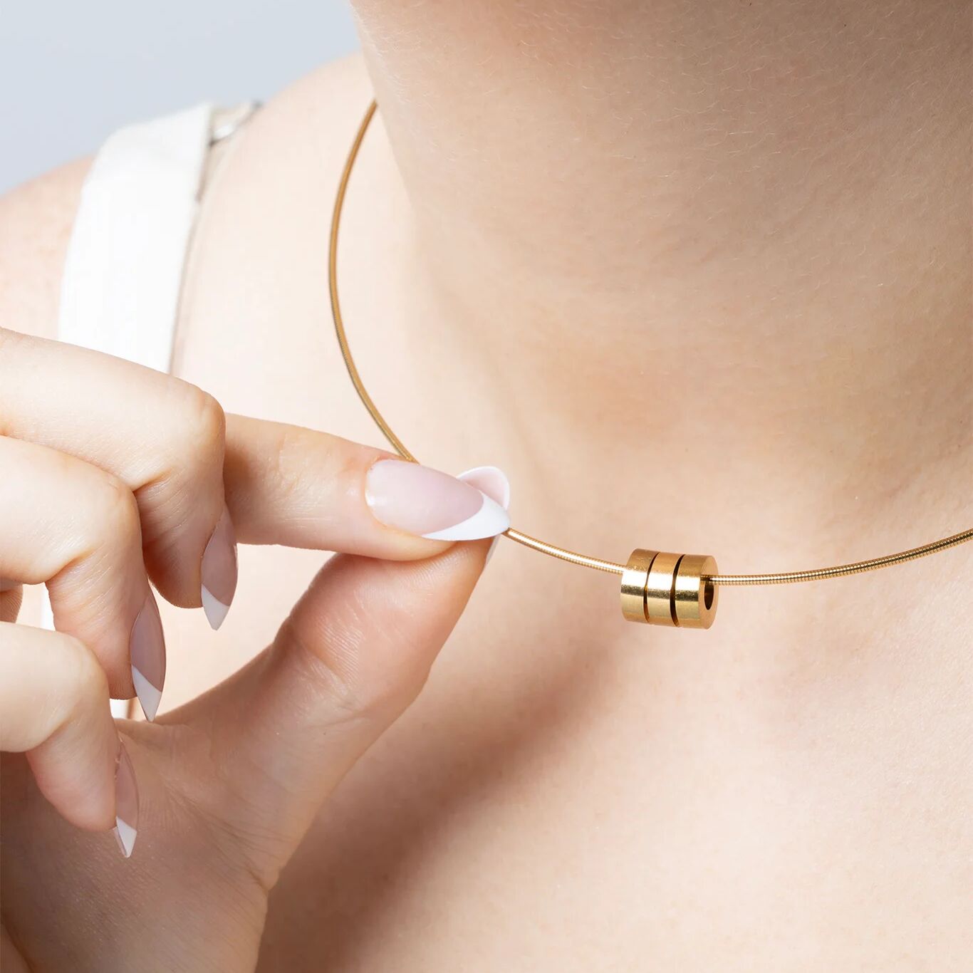 Gold necklace with spacer beads being adjusted on a person's neck with a neutral background