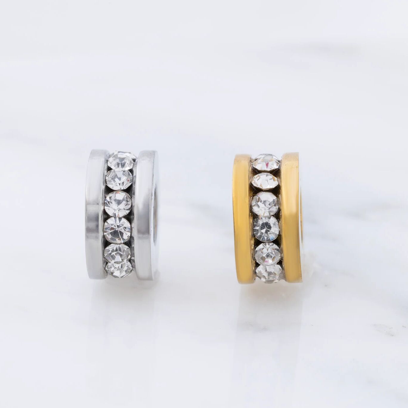 Two spacer beads, one gold and one silver, with embedded crystals on a light gray background.