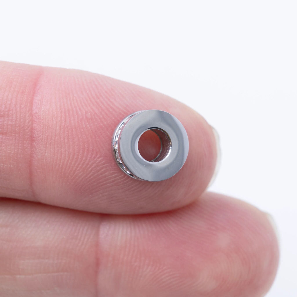 Silver spacer bead on a finger against a white background