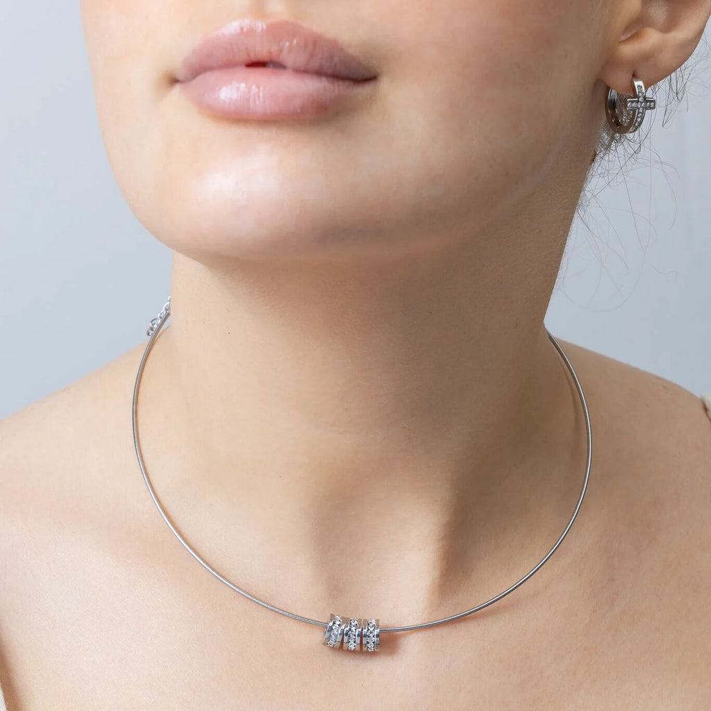 Close-up of a woman wearing a silver necklace with a small spacer beads on a neutral background