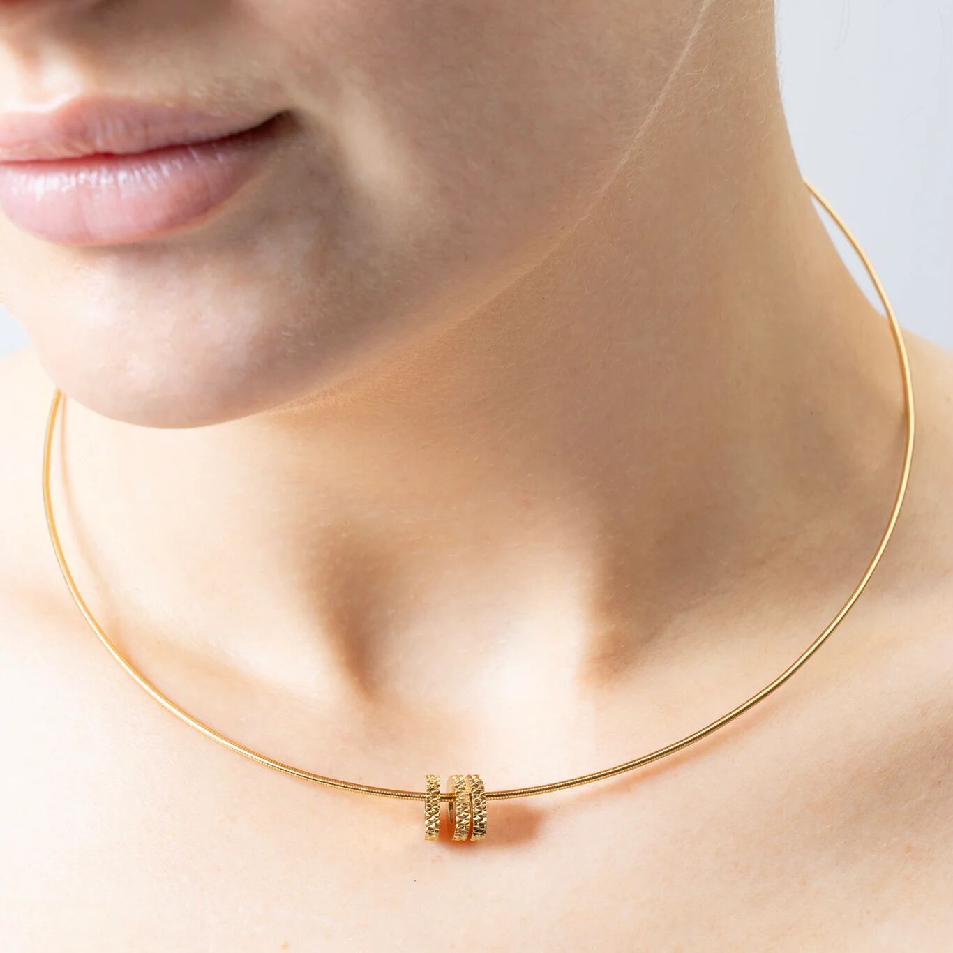 Gold necklace on a person's neck with a plain background