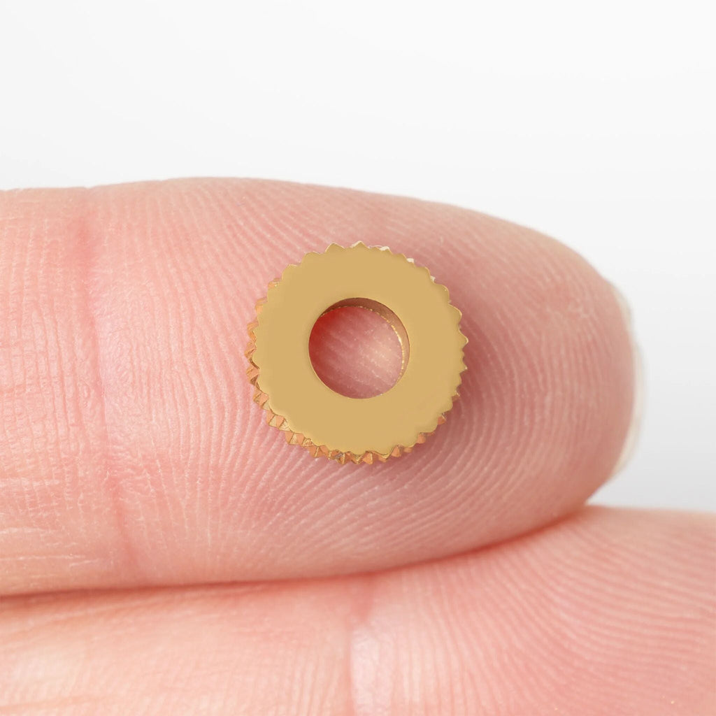 Gold textured spacer bead on a finger against a white background