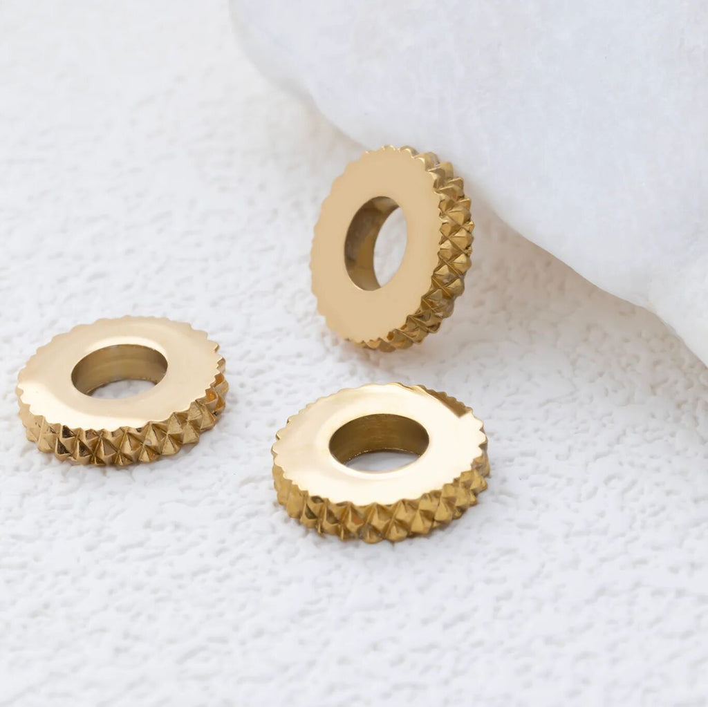 Three gold textured spacer beads on a white textured surface