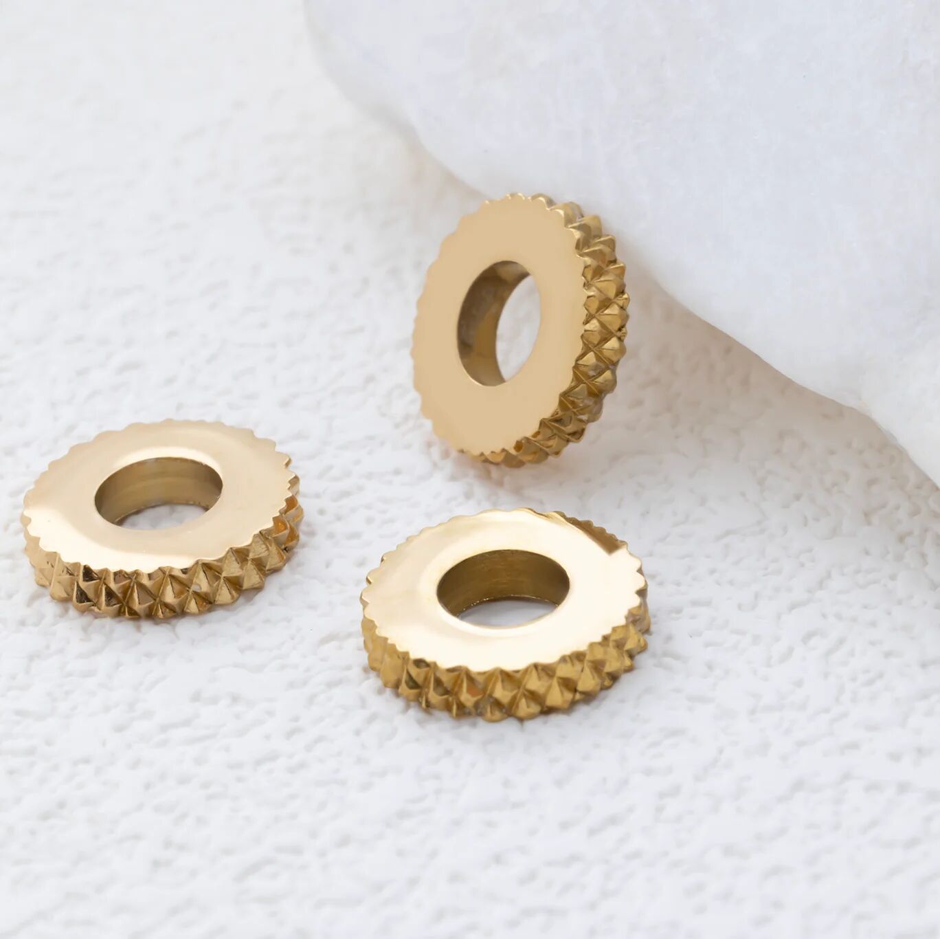 Three gold textured spacer beads on a white textured surface